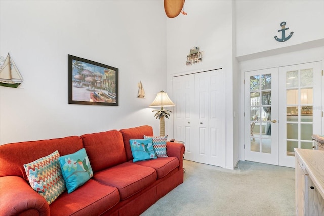 living area with light carpet, a towering ceiling, and french doors