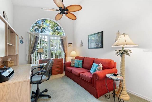 carpeted office space featuring ceiling fan, a towering ceiling, and baseboards