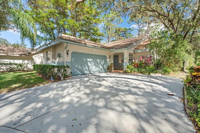 mediterranean / spanish house featuring driveway, an attached garage, a tiled roof, and stucco siding