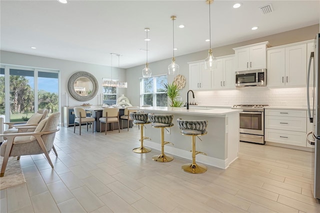 kitchen with appliances with stainless steel finishes, tasteful backsplash, pendant lighting, a center island with sink, and white cabinetry