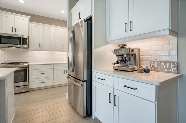 kitchen with light stone countertops, tasteful backsplash, stainless steel appliances, light hardwood / wood-style flooring, and white cabinetry