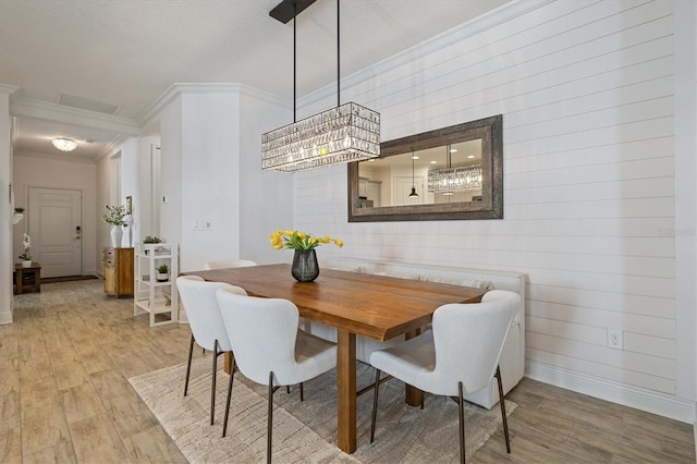 dining area featuring light wood-type flooring, crown molding, wooden walls, and a chandelier