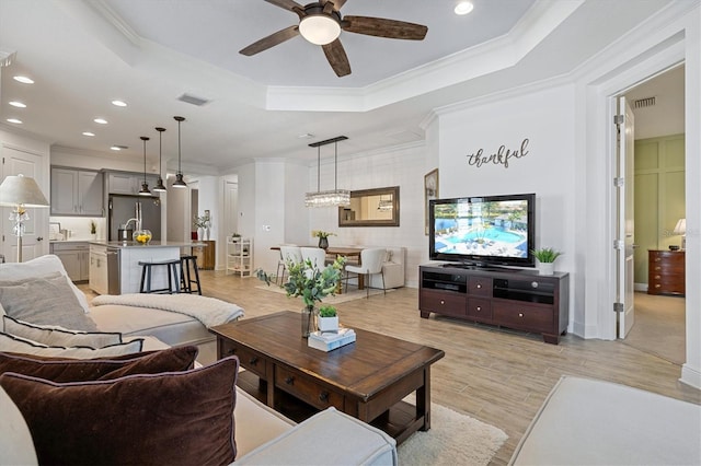 living room with ceiling fan, light hardwood / wood-style floors, a raised ceiling, and crown molding