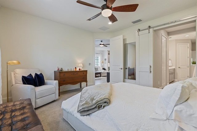 bedroom featuring ceiling fan, a barn door, light colored carpet, and ensuite bathroom