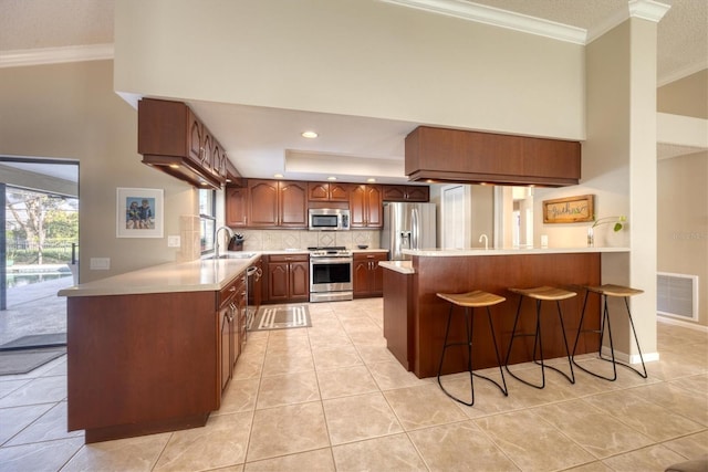 kitchen with sink, kitchen peninsula, a kitchen bar, light tile patterned floors, and appliances with stainless steel finishes