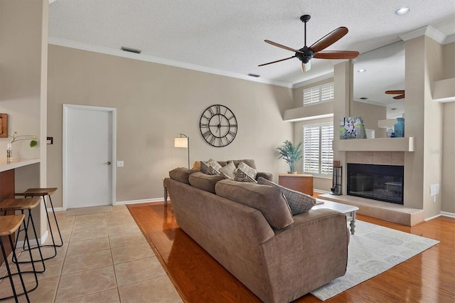 living room with crown molding, ceiling fan, a fireplace, a textured ceiling, and light hardwood / wood-style floors