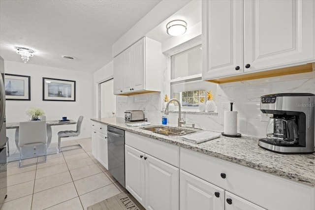 kitchen with light stone countertops, white cabinetry, sink, stainless steel dishwasher, and decorative backsplash