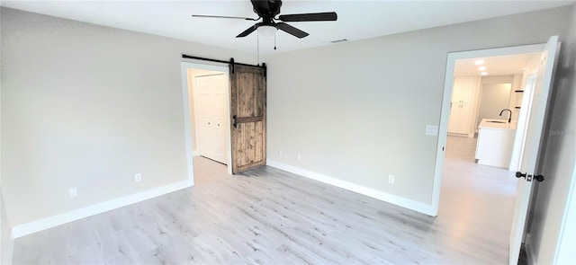 unfurnished bedroom with visible vents, ceiling fan, baseboards, a barn door, and light wood-style floors