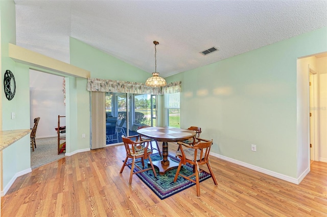 dining area with a textured ceiling, light hardwood / wood-style floors, and lofted ceiling