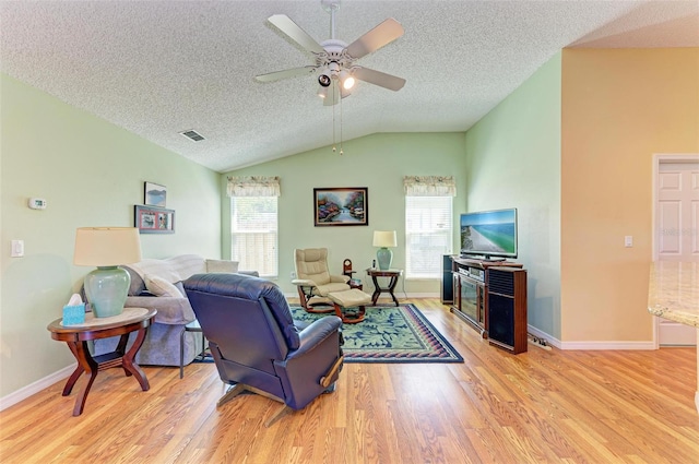 living room with ceiling fan, lofted ceiling, a textured ceiling, and light hardwood / wood-style flooring