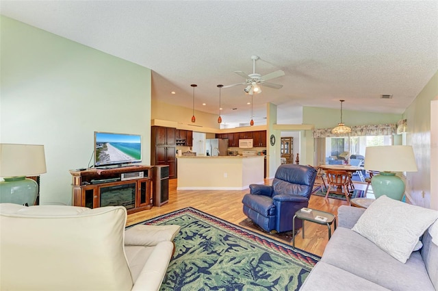 living room featuring a textured ceiling, light wood-type flooring, ceiling fan, and lofted ceiling