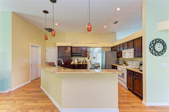 kitchen featuring white appliances, hanging light fixtures, an island with sink, dark brown cabinets, and light hardwood / wood-style floors