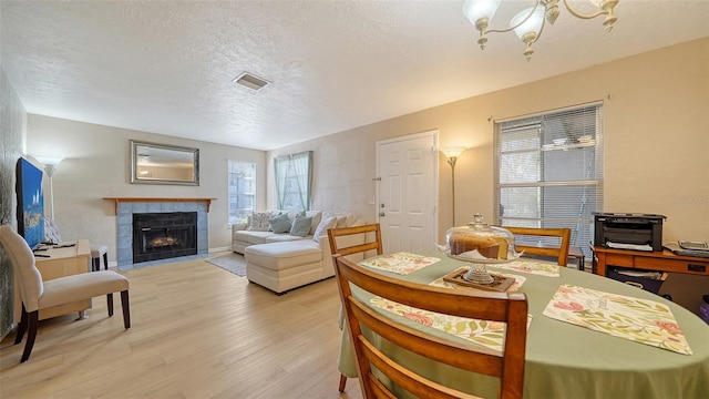 dining space with a tile fireplace, light hardwood / wood-style flooring, a textured ceiling, and a notable chandelier