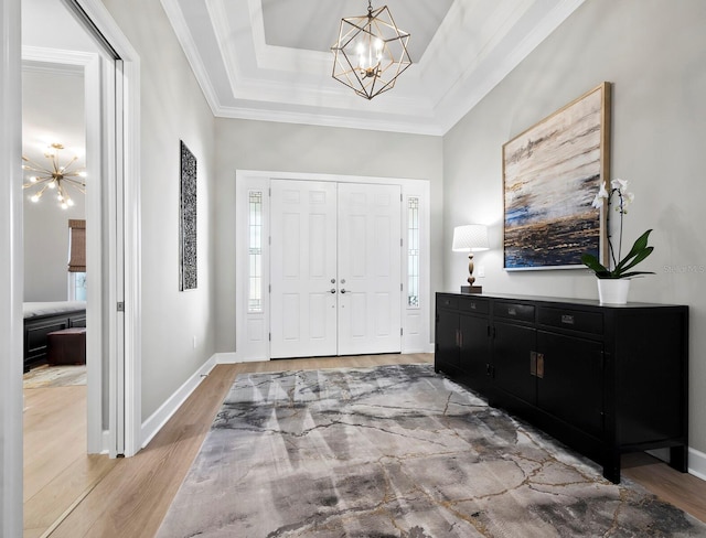 entryway with crown molding, light wood-type flooring, a tray ceiling, a healthy amount of sunlight, and a chandelier