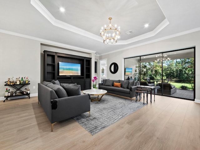 living room featuring a tray ceiling, light hardwood / wood-style flooring, a notable chandelier, and ornamental molding