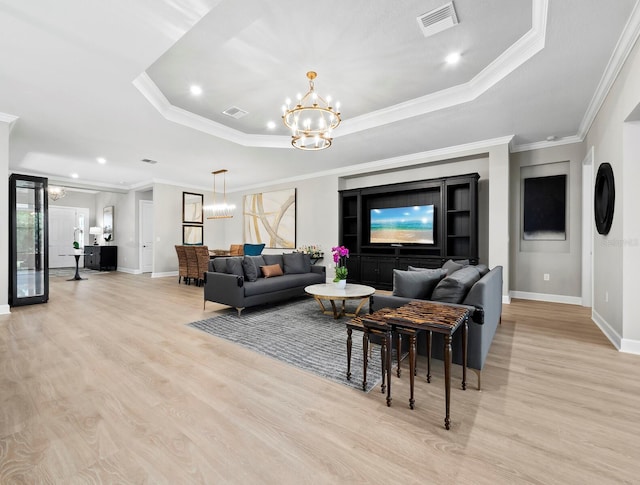 living room with a raised ceiling, light hardwood / wood-style floors, a notable chandelier, and ornamental molding