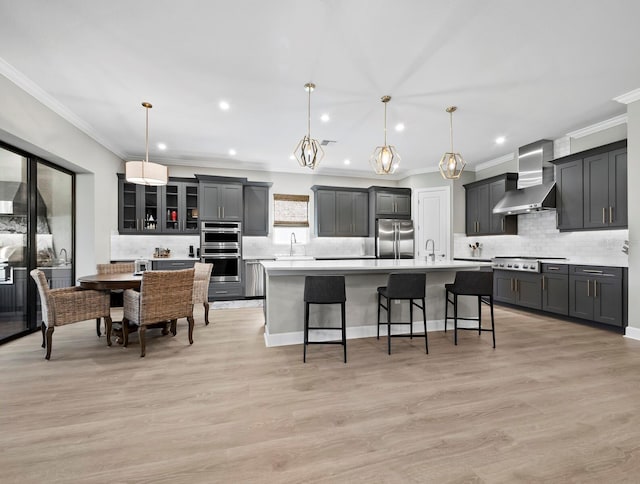 kitchen with sink, stainless steel appliances, hanging light fixtures, and wall chimney range hood