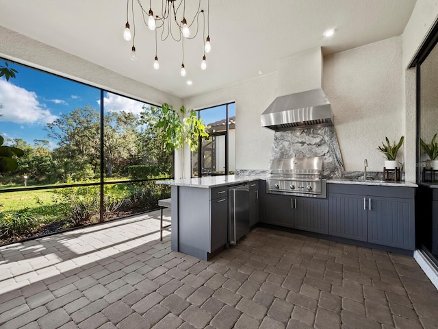 kitchen featuring kitchen peninsula, stainless steel fridge, wall chimney exhaust hood, sink, and a notable chandelier