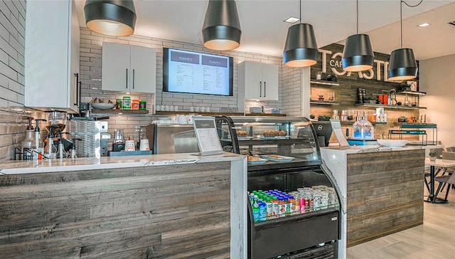 kitchen with kitchen peninsula, decorative backsplash, light stone counters, decorative light fixtures, and light hardwood / wood-style floors