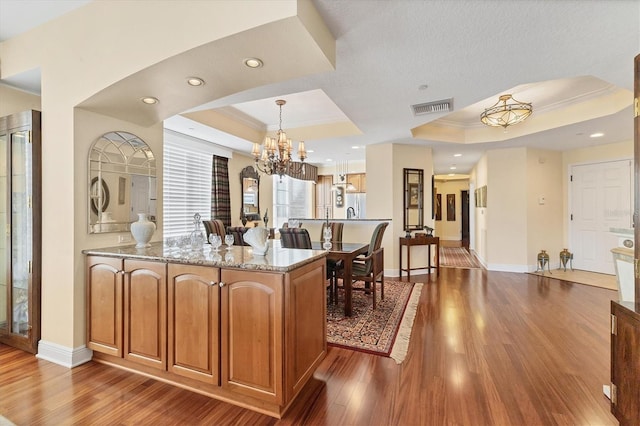 kitchen with a raised ceiling, light stone counters, a chandelier, decorative light fixtures, and light wood-type flooring