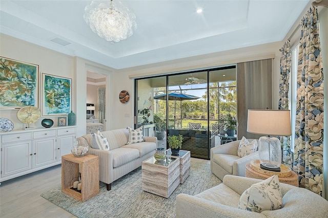 living room featuring an inviting chandelier, light wood-type flooring, and a tray ceiling