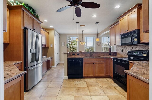 kitchen featuring light stone countertops, backsplash, sink, black appliances, and decorative light fixtures