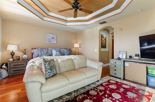 bedroom with hardwood / wood-style floors, a tray ceiling, ceiling fan, and ornamental molding