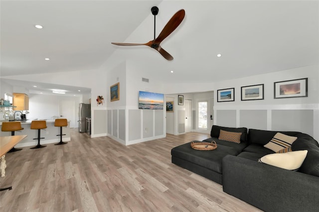 living room with ceiling fan, vaulted ceiling, and light wood-type flooring