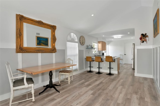 dining room featuring light wood-type flooring, lofted ceiling, and sink