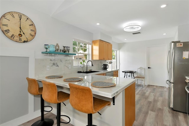 kitchen featuring a breakfast bar area, light hardwood / wood-style flooring, tasteful backsplash, kitchen peninsula, and stainless steel appliances