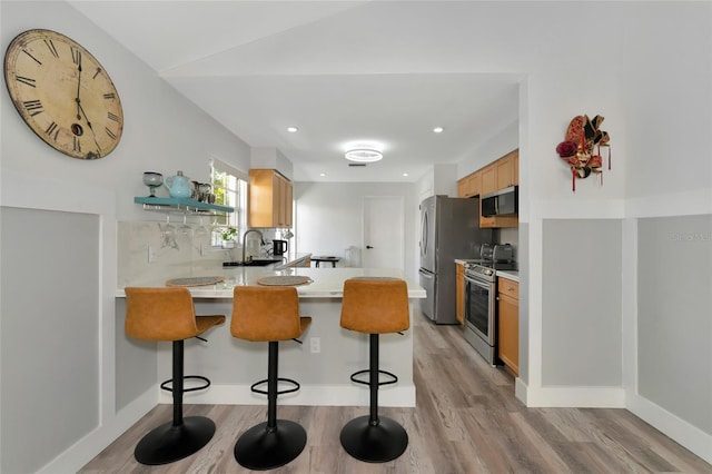 kitchen with kitchen peninsula, appliances with stainless steel finishes, light wood-type flooring, sink, and a breakfast bar area