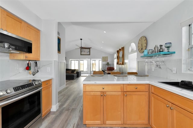 kitchen featuring appliances with stainless steel finishes, light wood-type flooring, vaulted ceiling, and backsplash