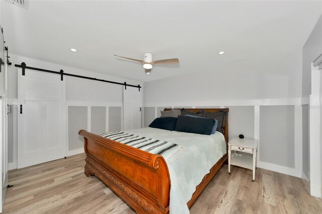 bedroom featuring a barn door, ceiling fan, and light hardwood / wood-style flooring