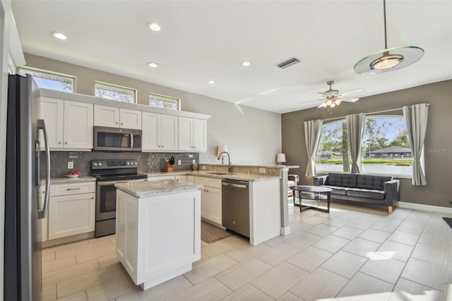 kitchen with kitchen peninsula, sink, appliances with stainless steel finishes, decorative light fixtures, and white cabinetry