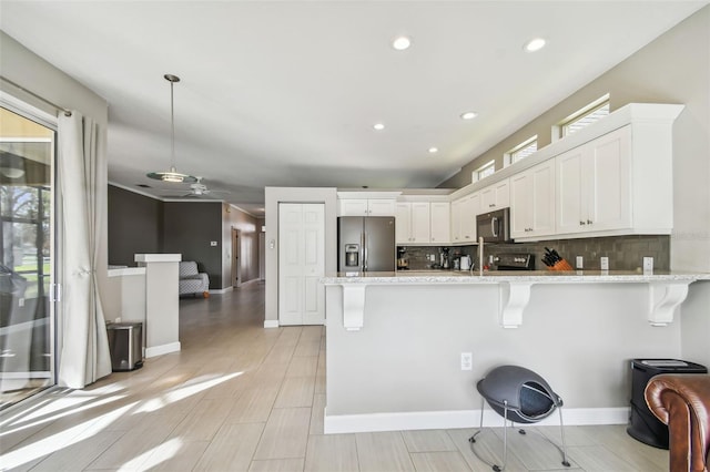 kitchen featuring kitchen peninsula, appliances with stainless steel finishes, a breakfast bar, white cabinets, and hanging light fixtures