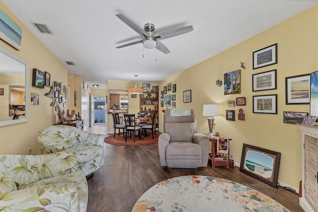 living room with ceiling fan, a textured ceiling, and dark wood-type flooring