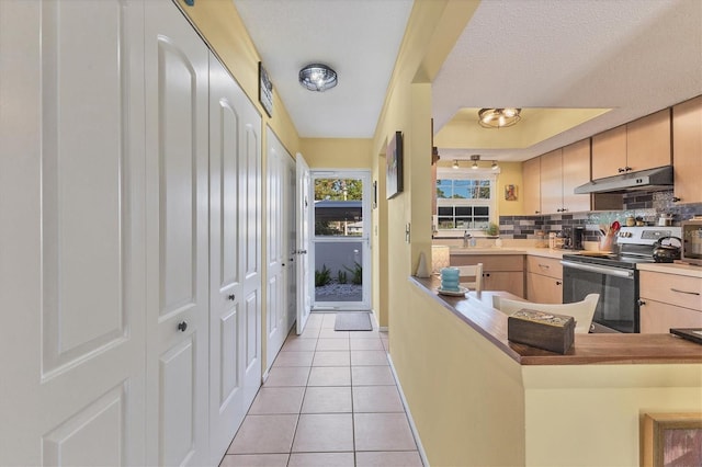 kitchen with light brown cabinets, light tile patterned floors, kitchen peninsula, decorative backsplash, and stainless steel range with electric cooktop