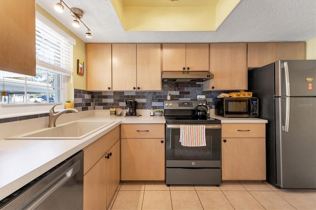 kitchen with under cabinet range hood, light brown cabinets, stainless steel appliances, and light countertops