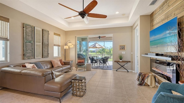 tiled living room with ceiling fan and a tray ceiling