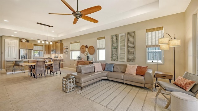 tiled living room with ceiling fan, plenty of natural light, and a tray ceiling