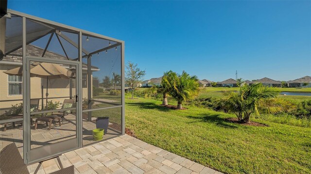 view of yard with a lanai, a water view, and a patio