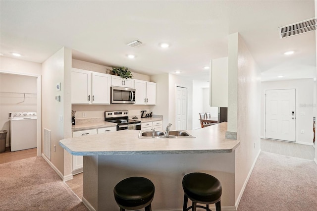 kitchen with a kitchen bar, light colored carpet, kitchen peninsula, stainless steel appliances, and washer / clothes dryer