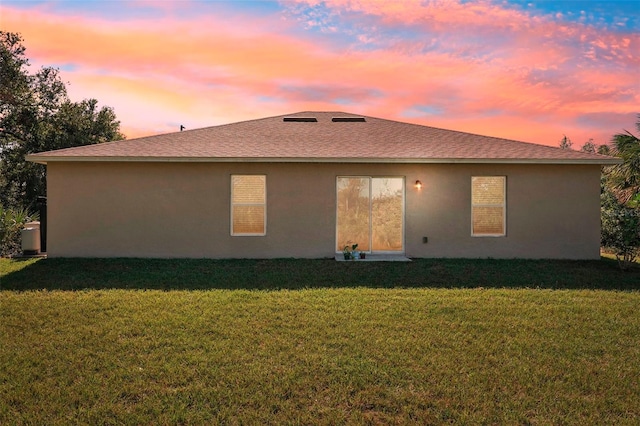 back house at dusk featuring a lawn