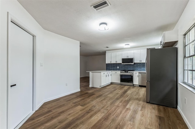 kitchen with white cabinets, appliances with stainless steel finishes, backsplash, kitchen peninsula, and hardwood / wood-style flooring