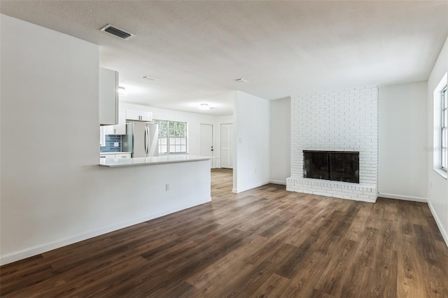 unfurnished living room with a brick fireplace, dark hardwood / wood-style floors, and a textured ceiling