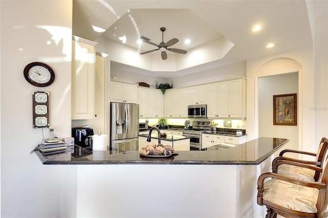 kitchen with ceiling fan, stainless steel appliances, a kitchen breakfast bar, kitchen peninsula, and a tray ceiling