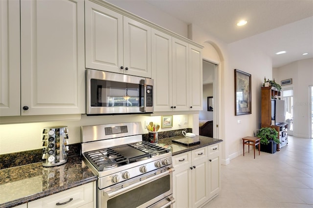 kitchen with dark stone countertops, white cabinets, light tile patterned floors, and appliances with stainless steel finishes