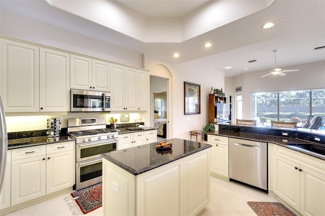 kitchen with ceiling fan, a kitchen island, appliances with stainless steel finishes, and dark stone counters