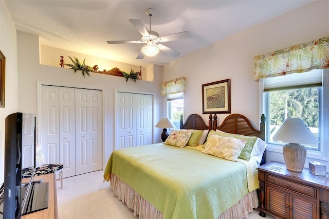 bedroom featuring multiple closets, light carpet, ceiling fan, and a textured ceiling