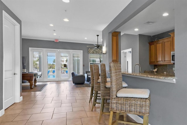 kitchen with kitchen peninsula, backsplash, light stone counters, a breakfast bar, and billiards